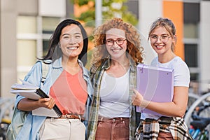 Diverse group of cheerful female college students standing outdoors, smiling