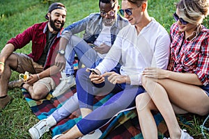 Diverse group of cheerful friends sitting on grass at sunset in nature park.