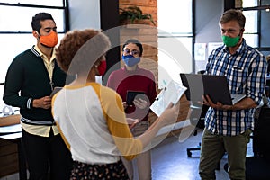 Diverse group of creative colleagues wearing masks having discussion in office