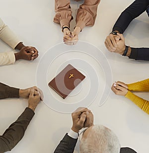 Diverse people sitting around table with the Holy Bible and praying to God together photo