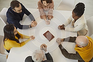 Religious people in Bible study group sitting around table and praying to God together