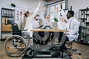 Diverse group of doctors smiling gesturing with arms raised after meeting