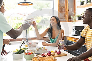 Diverse group enjoys a meal in a sunny kitchen, sharing laughter and drinks