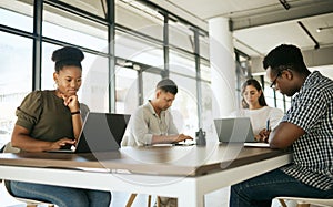 Diverse group of entrepreneurs business people working on laptops and writing notes while sitting around a table in a