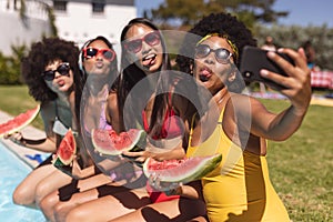 Diverse group of female friends taking selfie with watermelon sitting at the poolside