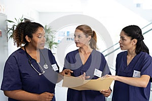 Diverse group of female healthcare workers with file talking in hospital corridor