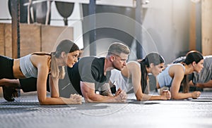 Diverse group of fit people doing bodyweight plank hold exercises together in a gym. Focused athletes training to build