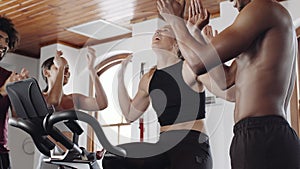 Diverse group of fit young adults supporting Caucasian female friend while she cycles on stationary exercise bike at an