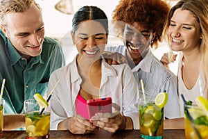 Diverse group of friends enjoying mojito drink while using phone at beach bar