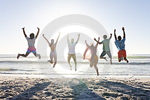 Diverse group of friends jumping joyfully on a sunny beach