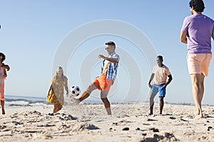 A diverse group of friends, young adults, enjoy a casual game of soccer on the beach
