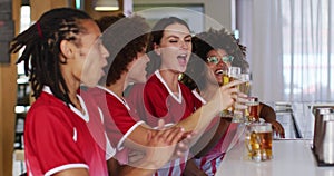 Diverse group of happy friends watching a game raising glasses making a toast at a bar