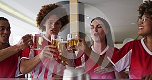 Diverse group of happy friends watching a game raising glasses making a toast at a bar