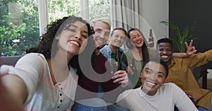 Diverse group of happy male and female friends smiling and taking selfie in living room