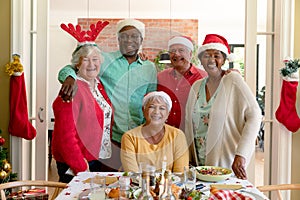 Diverse group of happy senior friends in holiday hats celebrating christmas together, taking photo