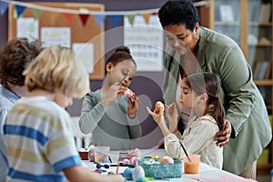 Diverse group of little kids painting Easter eggs enjoying arts and crafts class