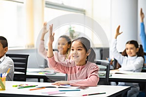 Diverse group of little school children raising hands at classroom