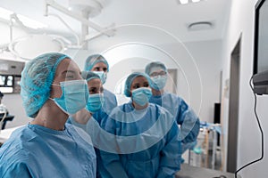 Diverse group of male and female surgeons in operating theatre wearing face masks looking at screen