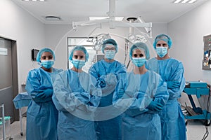 Diverse group of male and female surgeons standing in operating theatre wearing protective overalls