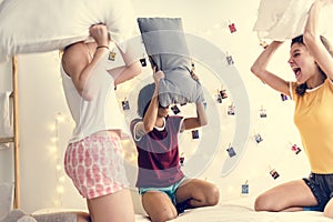 A diverse group of women playing pillow fight on bed together