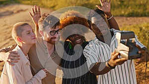 Diverse group of young adult friends posing together for selfie with vintage instant camera. Camping. Horizontal outdoor