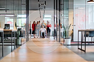 A diverse group of young business people walking a corridor in the glass-enclosed office of a modern startup, including