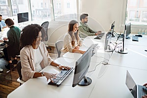 A diverse group of young professionals are engaged in their respective tasks on the computers