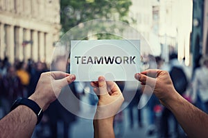 Diverse hands holding together a paper with teamwork text. Group of three people unity and team concept as business metaphor for