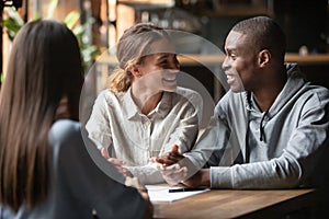 Diverse happy couple sitting at table with real estate agent