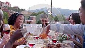 Diverse happy friends having dinner party outside at rooftop terrace.