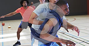 Diverse male basketball players dribbling ball and blocking during game at indoor court, slow motion