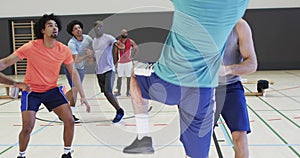 Diverse male basketball players dribbling and shooting ball during game at indoor court, slow motion