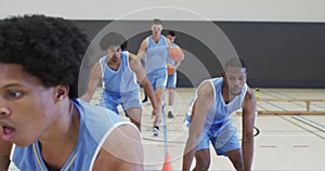 Diverse male basketball team training, dribbling with balls at indoor court, slow motion