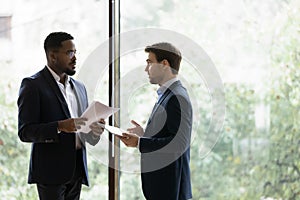 Diverse male business partners discuss paperwork in office