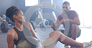 Diverse male coach motivating determined woman exercising with medicine ball at gym, in slow motion