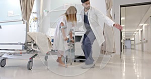 Diverse male doctor helping girl patient use crutches in hospital ward, slow motion