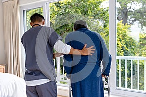 Diverse male doctor helping senior male patient using crutches at home