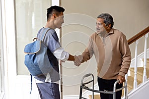 Diverse male doctor and senior male patient with crutches shaking hands at home