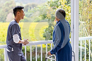 Diverse male doctor and senior male patient using crutches looking out window at home