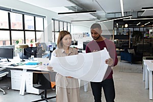 Diverse male and female colleague looking at blueprints and discussing