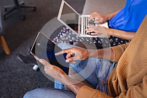 Diverse male and female colleagues working sititng on sofa in office using blank computer and tablet