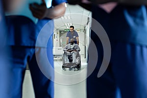 Diverse male healthcare worker pushing african american male patient in wheelchair in hospital