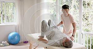 Diverse male physiotherapist advising and senior male patient exercising on couch, in slow motion