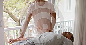Diverse male physiotherapist advising and senior male patient exercising on couch, in slow motion