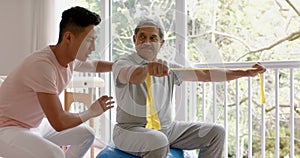 Diverse male physiotherapist advising and senior male patient using exercise band, in slow motion