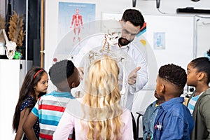 Diverse male teacher and elementary schoolchildren studying skeleton in biology class