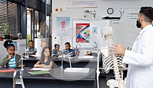 Diverse male teacher and elementary schoolchildren studying skeleton in biology class