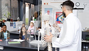 Diverse male teacher and elementary schoolchildren studying skeleton in biology class