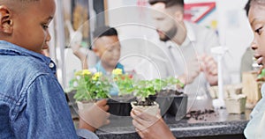 Diverse male teacher and happy schoolchildren studying plants and wind turbines in school classroom