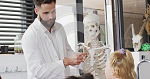 Diverse male teacher and happy schoolchildren studying skeleton in biology class